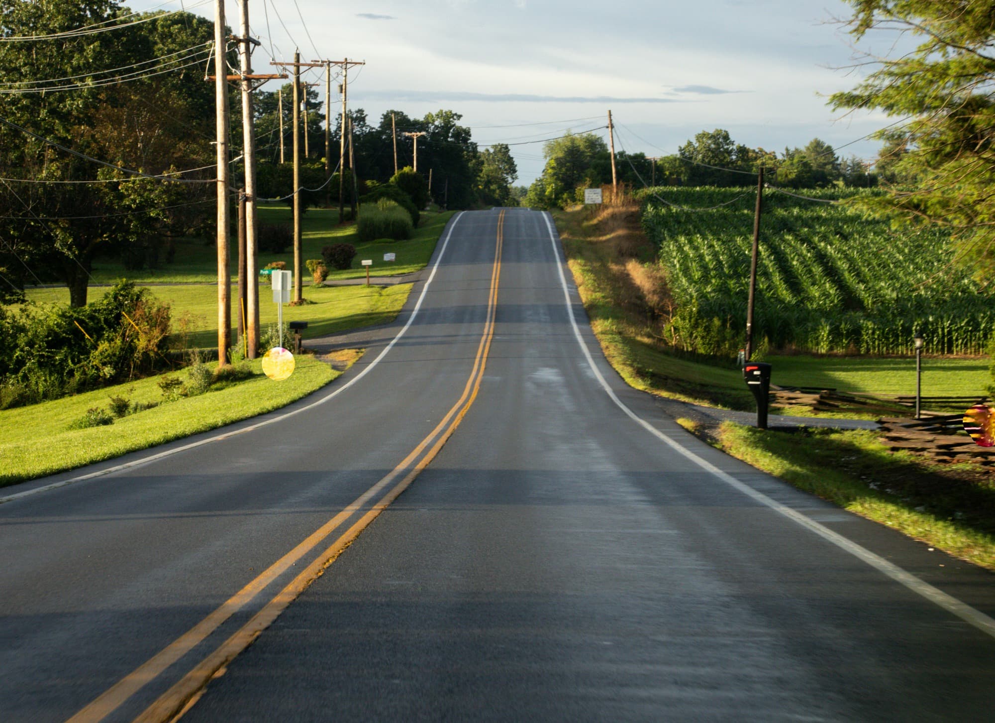 Image of a road with electrical poles on one side and a farm field on the other
